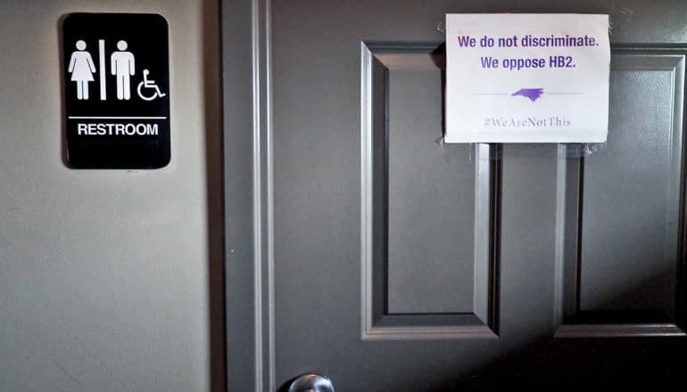 all-gender bathroom sign and poster denouncing HB-2