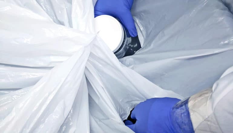 gloved hands put jar through holes in trash bag