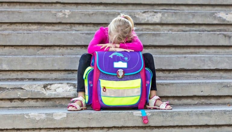 girl on steps rests head on backpack