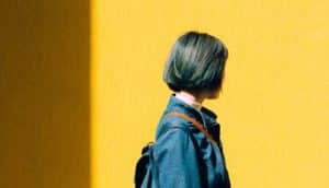 woman looks away walking in front of yellow wall