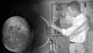 man stands to right of projector with moonscape on sphere