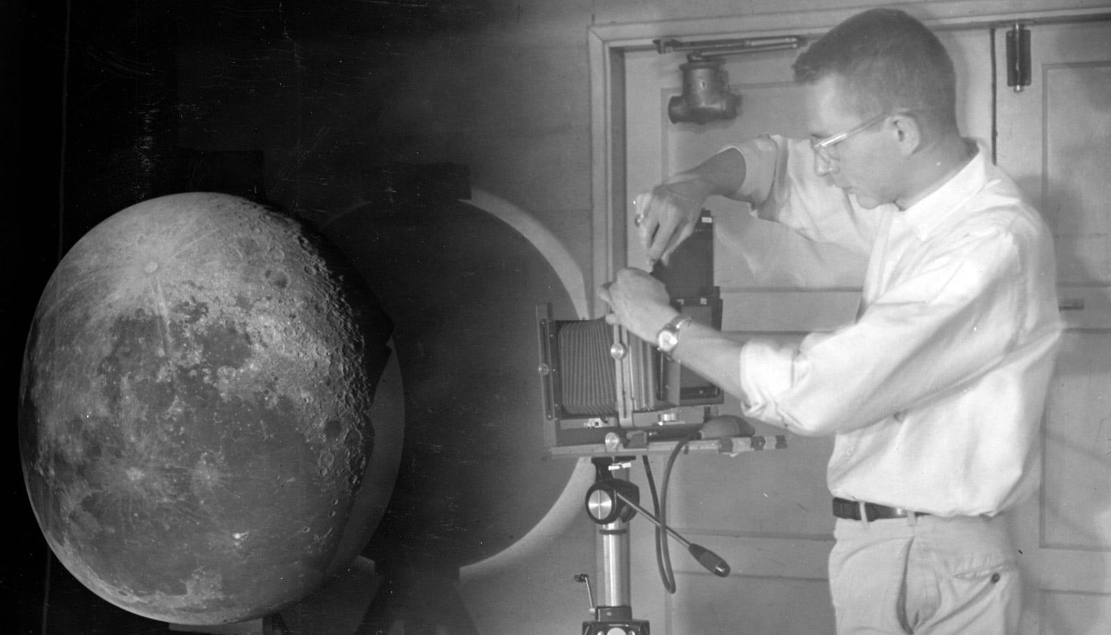 man stands to right of projector with moonscape on sphere