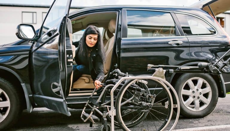ableism concept - woman with disabilities leans out of car toward wheelchair