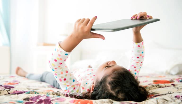 girl holds tablet while lying down - children's tv