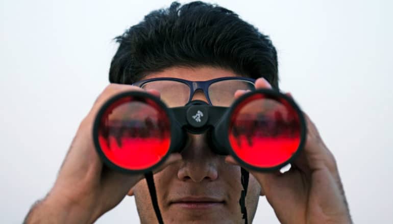 man uses binoculars with red lenses