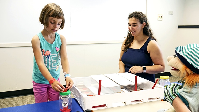 A girl places coins in her "bank" during the "trust" experiment involving a puppet