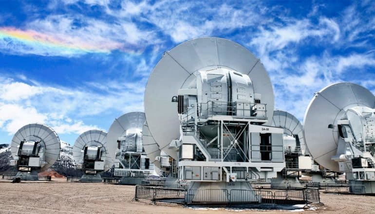 The images show the Atacama Large Millimeter Array (ALMA) of radio dishes facing away against a blue sky. (cloaked black hole concept)