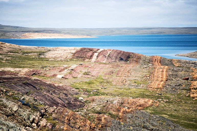 A huge expanse of rock shows different colored streaks, with water sitting just over a rocky ridge