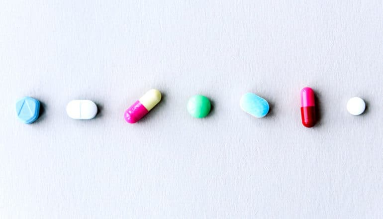 row of colorful pills on white paper - adverse drug reactions