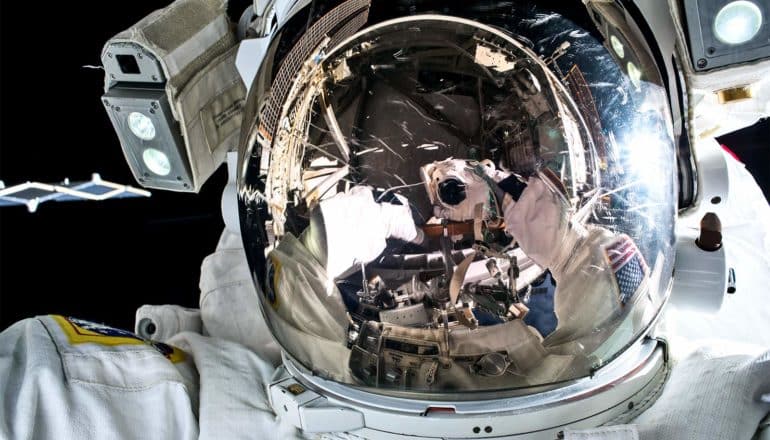 an astronaut's helmet shows the reflection of the astronaut taking a self-portrait photograph.