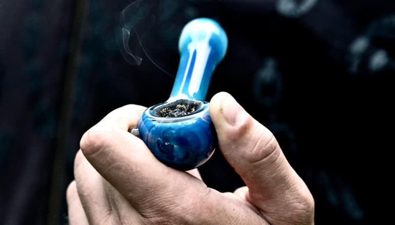 hand holds blue glass pipe for smoking marijuana
