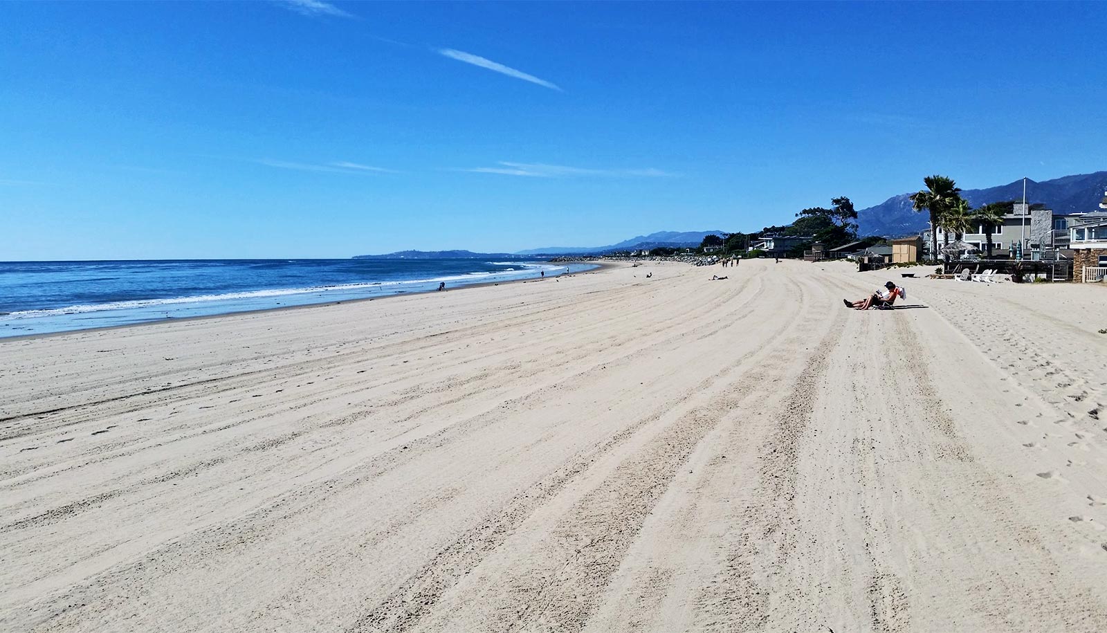 The image shows Carpinteria City Beach, with flat, groomed sands and blue sky.