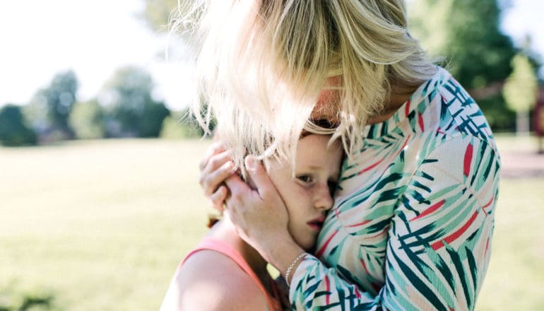 woman consoles preteen girl by holding her close, hands on her head