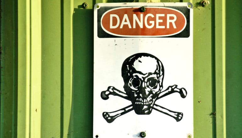 A sign that reads "Danger" and shows a skull and cross bones hangs on a green wall