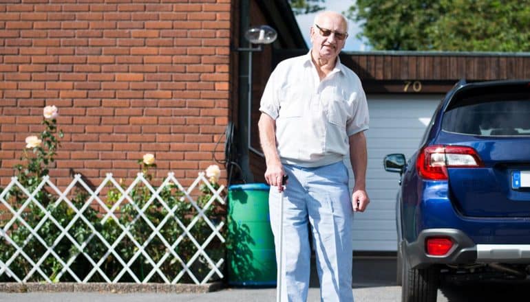 elderly man stands in driveway next to car