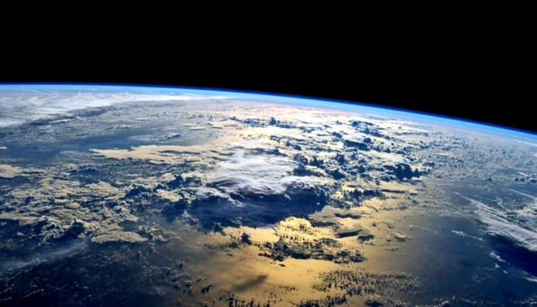 The curve of the Earth shows up bright blue against the blackness of space, with huge clouds visible in the atmosphere