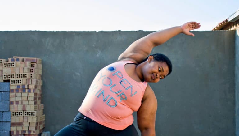 black woman in "open your mind" shirt does yoga bend on rooftop