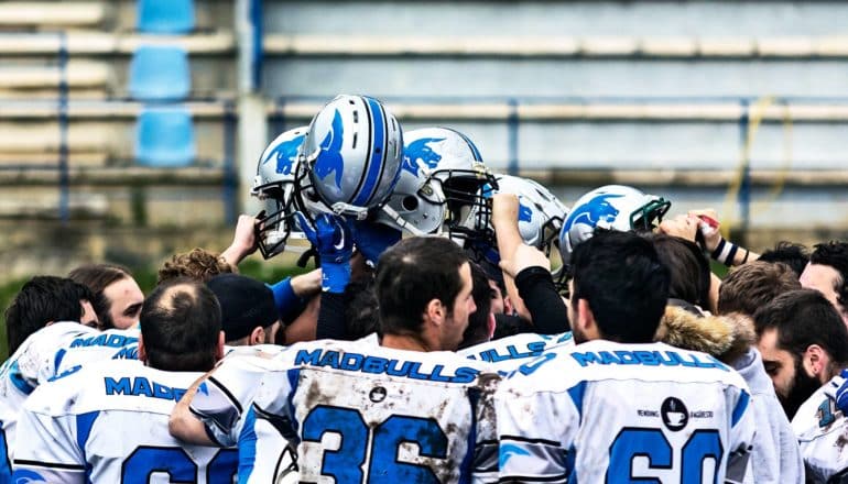 The image shows a football team holding up their helmets while in a huddle. (midbrain concept)