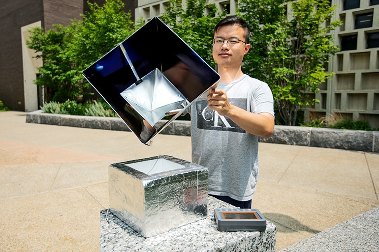 Zhou holds the solar shelter removed from a smaller box to show its insides, a darkly reflective interior in which a reflective panel is suspended