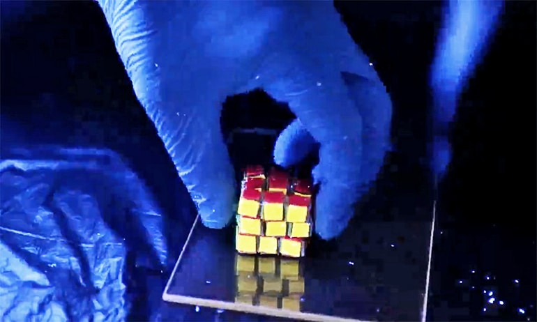 The image shows a researcher picking up the hydrogel Rubik's Cube-like structure.