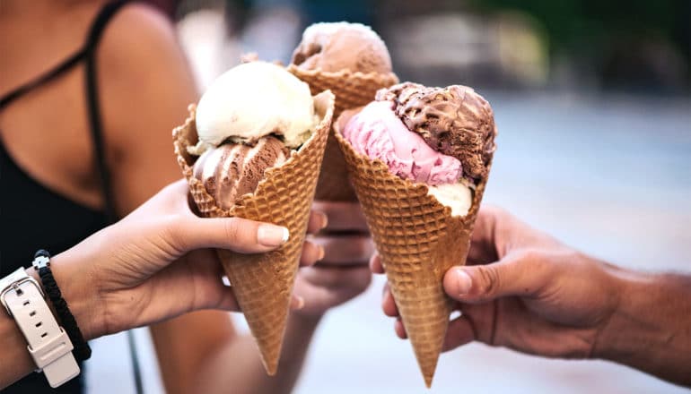 3 friends hold up their ice cream cones with different flavors as if to say, "Cheers!"
