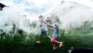 The image shows kids running through smoke in a backyard. (asthma concept)