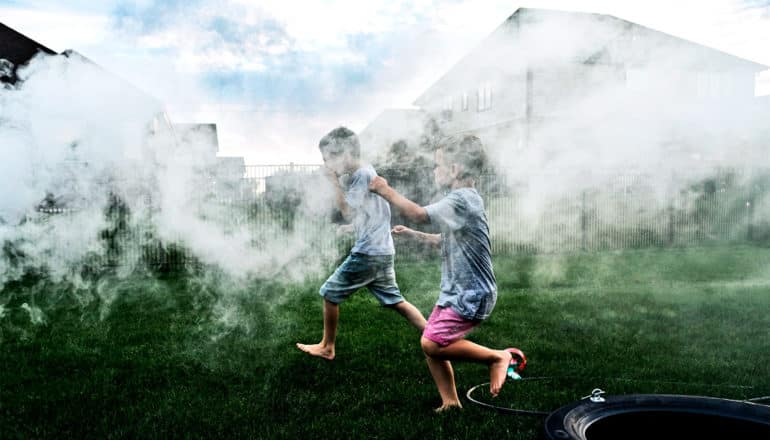 The image shows kids running through smoke in a backyard. (asthma concept)