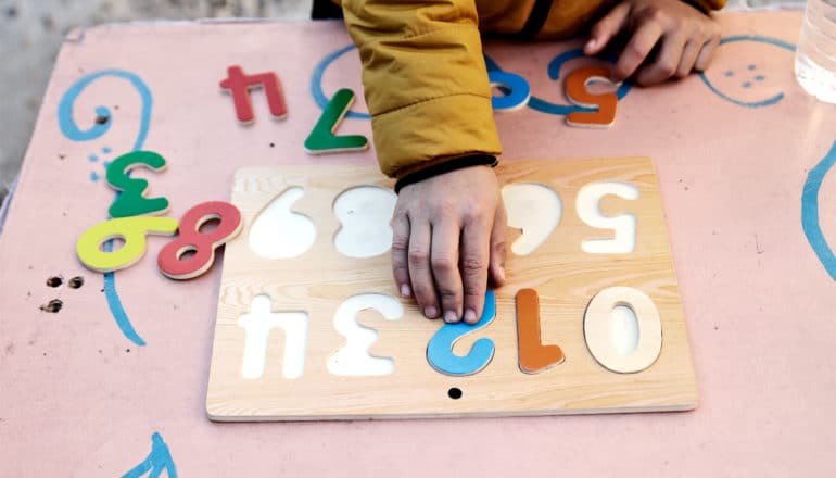 The image shows a kindergartener playing with a toy involving placing number blocks in the right order. (kindergarten concept)