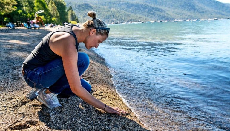 A researcher kneels on the shore of Lake Tahoe. (microplastics concept)