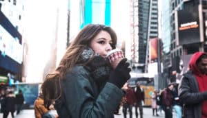 A young woman drinking a coffee in New York City listens as people pass her on the street