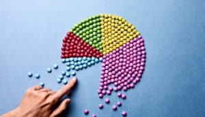 A hand moves small, colorful candies into a larger whole that looks like a pie chart with different colored segments.