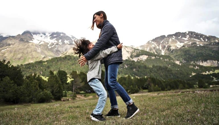 mom and kid frolic in front of mountainscape