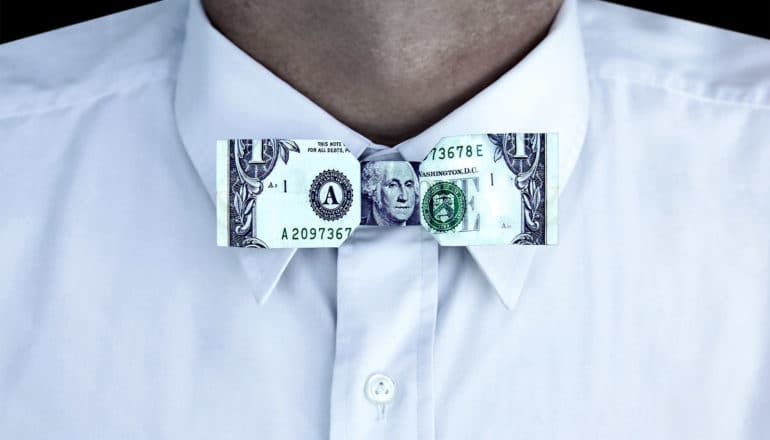 A man in a white dress shirt wears a bowtie made with a dollar bill