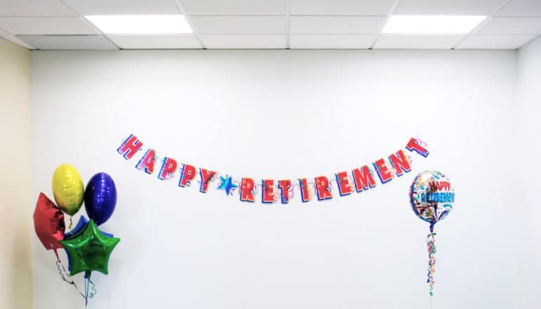 "happy retirement" banner on wall and balloons in otherwise blank room with panel ceiling and fluorescent lights