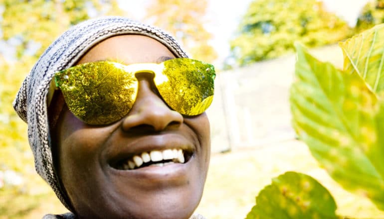 greenery reflects in the sunglasses of a smiling person