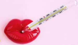 A pair of plastic lips sits on a pink background with a thermometer sticking out