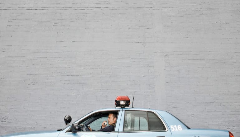 officer in police car which appears very low in frame against gray wall