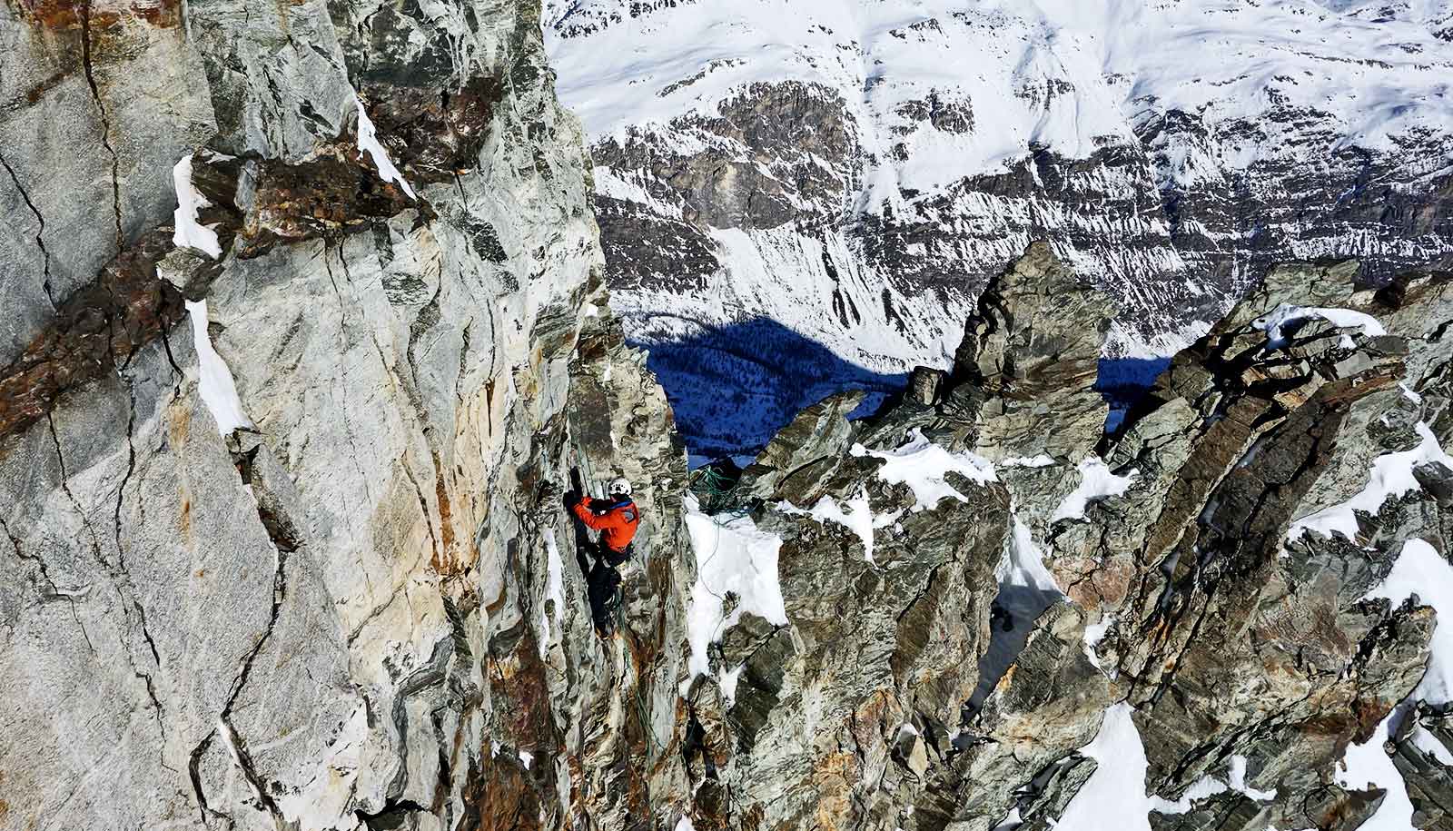 Jan Beutel climbs the massive mountain in a red jacket and safety gear, his body tiny against the scope of the Matterhorn