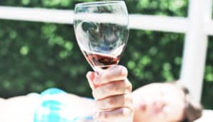 woman holds up her wine glass to the camera while lying down in a swimsuit. (resveratrol concept)
