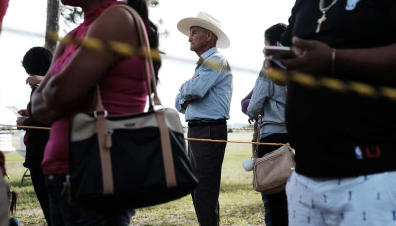 diverse group of people in line, focus on older person in cowboy hat at center