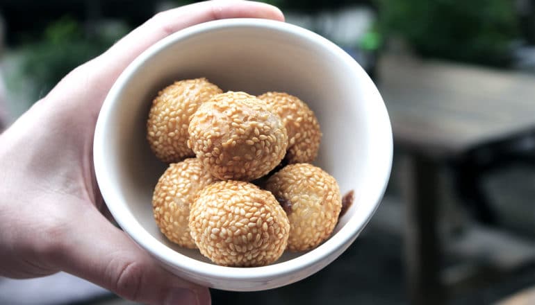 The image shows sesame balls in a white bowl. (sesame allergy concept)