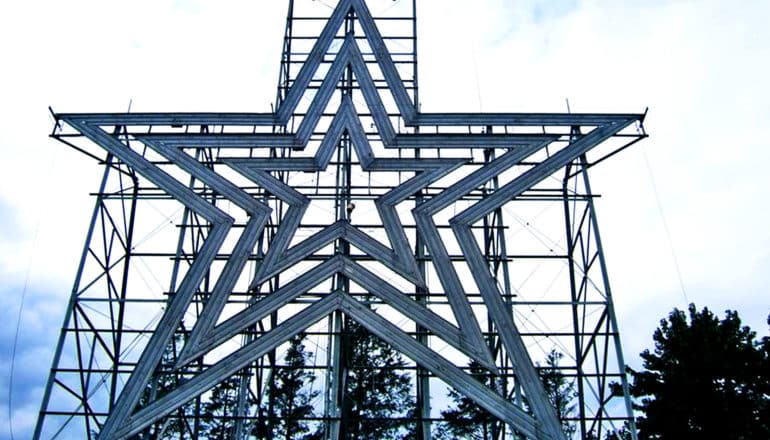 The image shows a large star-shaped structure standing up with scaffolding against a cloudy sky. (neutron stars concept)