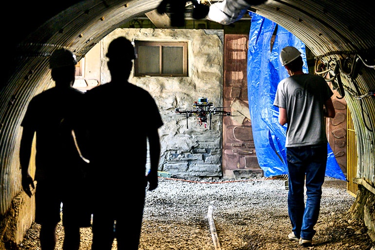 Researchers piloting the drone robot leave the Tour-Ed mine, walking from the dark mine into the light outside.