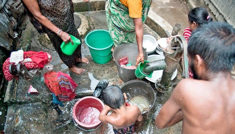 people and colorful buckets crowd around a water pump