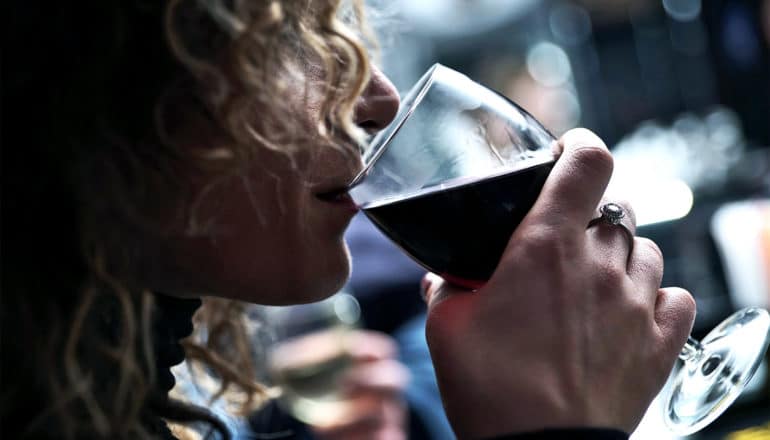 A woman with curly hair sips a glass of red wine