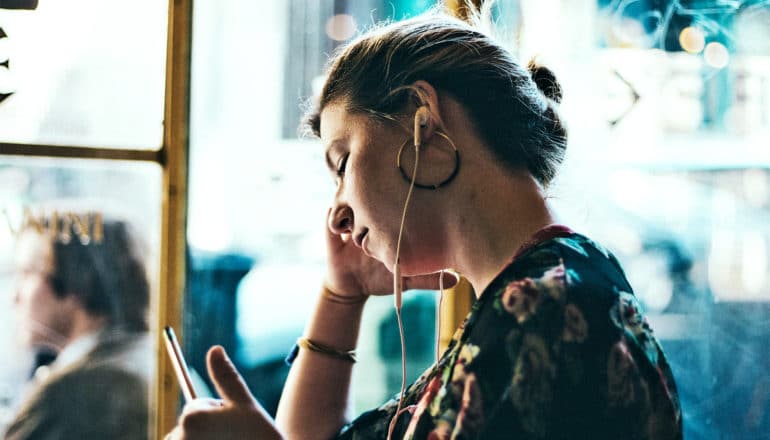 A woman leans on her hand and closes her eyes while listening to headphones sitting in a cafe