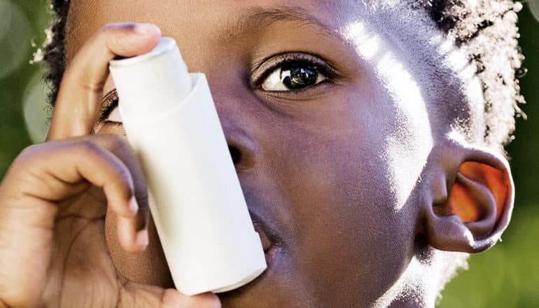 A young boy uses a white inhaler as the sun shines on his face