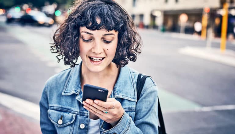 The image shows a young woman using phone on the street. (voting online concept)