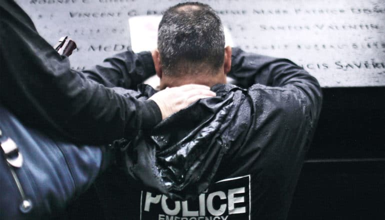 A man in a black rain jacket that reads "Police Emergency" kneels at the memorial at ground zero in New York City as another person puts their hand on his back