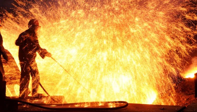 steel worker holds hose in shower of molten iron sparks